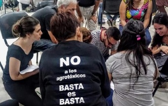 Habitantes de San Jose en reunion, en primer plano una persona con remera negra y una leyenda en la espada que dice: No a los agrotoxicos, basta es basta