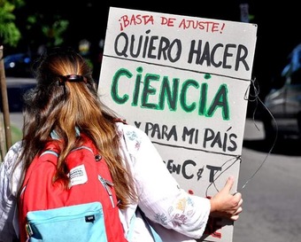 Mujer de espaldas con un cartel que dice:  Basta de ajuste, quiero hacer ciencia para en y para  mi país