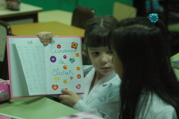 Imagen de la película "El vaivén de las escuelas" en la que se ven dos nenas con guardapolvo en la escuela, una de ellas mostrando su cuaderno.