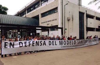Estudiantes y docentes en la puerta de la facultad con una bandera Excatas en defensa del modelo sanitario de farmacia