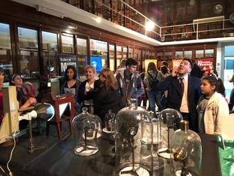 Visitantes en el museo de fisica obsevando experimentos,  salon recubierto de viejas estanterias de madera con viejos elementos de trabajo