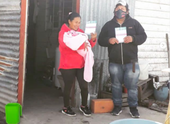 pareja con bebe mostrando carnet de vacunación en la puerta de su casa